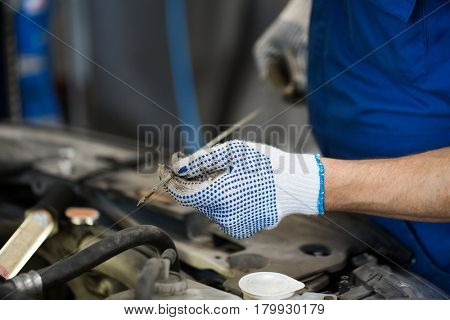 car service, repair, maintenance and people concept - auto mechanic man with dipstick and lamp checking for motor oil level at workshop