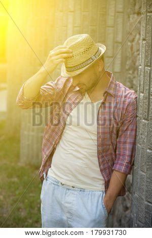 Portrait of man in straw hand. Handsome man posing near brick wall and looking somewhere below. Toned image.