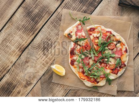 Italian pizza with salami cherry tomato mushrooms and arugula on wooden table with copy space