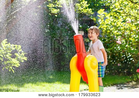 Active preschool kid boy  playing and splashing with a garden hose on hot and sunny summer day. Child having fun outdoors. Funny outdoors leisure wth water for children.