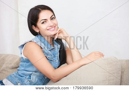 Relaxed casual brunette in blue cardigan and In blue jeans sits on the couch in bright living room