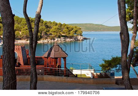 Brown playground near deep blue sea and rocky coast with green forest pine trees and hills on the back. Bozava Croatia summer