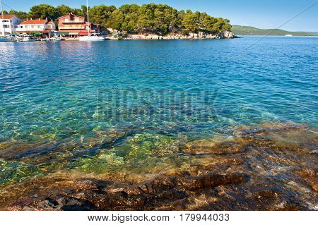 Transparent deep blue sea water rocky coast and rocky bottom green forest and hills on the back. Several colorful houses and white yachts near the beach. Bozava Croatia summer