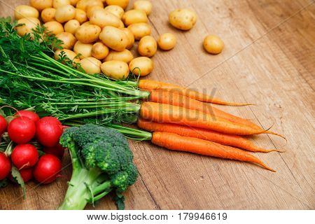 Potatoes with carrot. Red radish, brocoli and raw new potato. Fresh natural vegetables. Organic bio food. On wooden table.