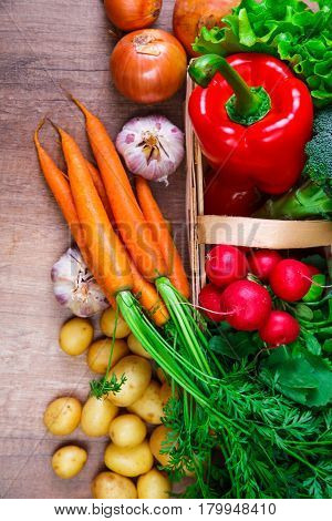 Vegetables. Potatoes, carrot and red pepper. Lettuce salad, garlic and brocoli. Onion and radish. Wooden basket on rustic table.