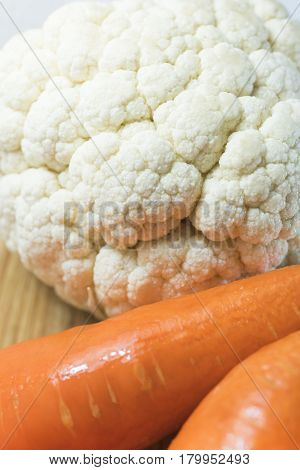 fresh white cauliflower and orange carrots on a brown wood cutting board.Heatlh vegan food concept