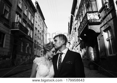 Romantic sensual couple of newlyweds posing outdoors in old european street family portrait of handsome groom hugging smiling bride