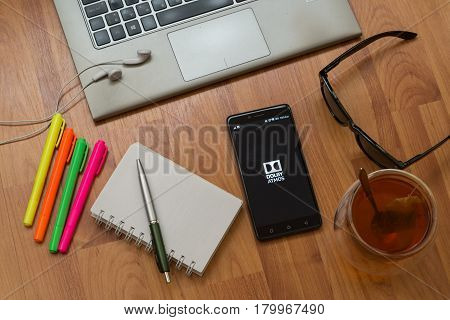 Nitra, Slovakia, april 3, 2017: Dolby Atmos application in a mobile phone screen. Workplace with a laptop, an earphones, notepad, pen, tea, sunglasses and color markers on wooden background