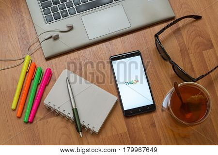 Nitra, Slovakia, april 3, 2017: Badoo application in a mobile phone screen. Workplace with a laptop, an earphones, notepad, pen, tea, sunglasses and color markers on wooden background
