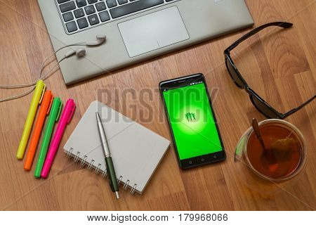 Nitra, Slovakia, april 3, 2017: Pocketbook application in a mobile phone screen. Workplace with a laptop, an earphones, notepad, pen, tea, sunglasses and color markers on wooden background