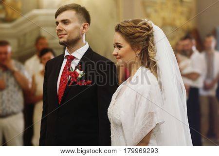 Emotional couple during wedding ceremony handsome happy groom and beautiful bride tearing up during priests speech at wedding ceremony in christian church