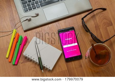 Nitra, Slovakia, april 3, 2017: Instagram application in a mobile phone screen. Workplace with a laptop, an earphones, notepad, pen, tea, sunglasses and color markers on wooden background