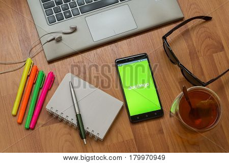 Nitra, Slovakia, april 3, 2017: Duolingo application in a mobile phone screen. Workplace with a laptop, an earphones, notepad, pen, tea, sunglasses and color markers on wooden background