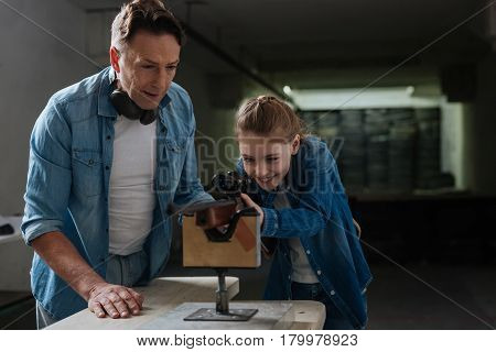 Family relations. Pleasant caring nice father standing near his daughter and teaching her how to shoot while spending time with her