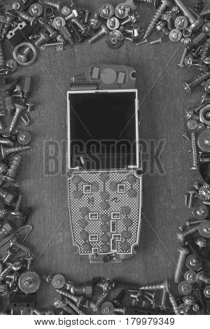 frame made of screws, bolts on a desk around broken cell mobile phone in black and white