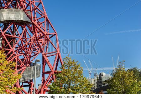 London England - October 17, 2016; From Queen Elizabeth Olympic Park in Stratford London abstract ArcelorMittal Orbit red tubular spiralling steel structure on one side of image with white construction cranes in ditstant city skyline.