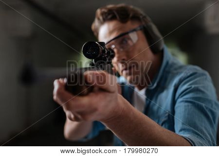 Professional shooter. Handsome professional male sniper holding a gun and looking into the optical sight while choosing the target