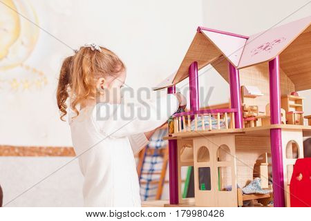 Beautiful little girl playing with a wooden dollhouse