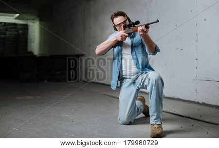 Absolute accuracy. Skilled confident nice man wearing protective equipment and holding a gun while hitting the aim