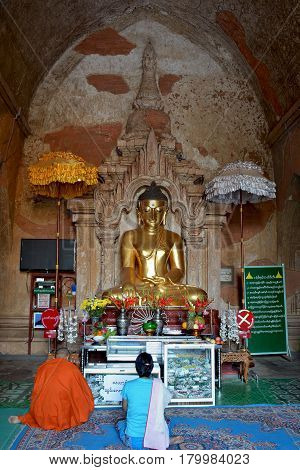 Buddhist Monk And Myanmar Woman Praying To Lord Buddha Golden Statue Inside Ancient Temple In Bagan,