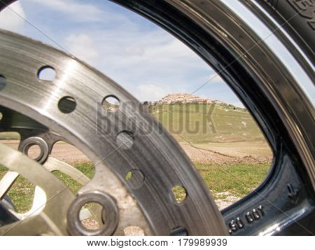 Italy Castelluccio di Norcia - april 24 2015: Image of Castelluccio shot through the hoop front wheel of the motorcycle. The motorcycle is located on the roadside overlooking the floor dedicated to the cultivation of lentils