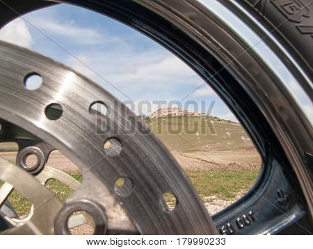 Italy Castelluccio di Norcia - april 24 2015: Image of Castelluccio shot through the hoop front wheel of the motorcycle. The motorcycle is located on the roadside overlooking the floor dedicated to the cultivation of lentils