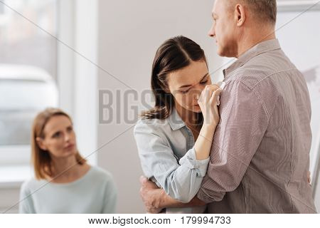 Overcome your fear. Sad female leaning her right arm on the strong shoulder of her coworker looking downwards while being present at consultation