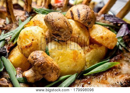 Grilled potatoes and mushrroms with meat and herbs close up.