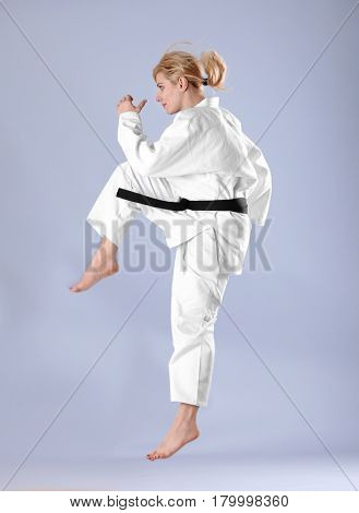 Young sporty woman practicing martial arts on light background