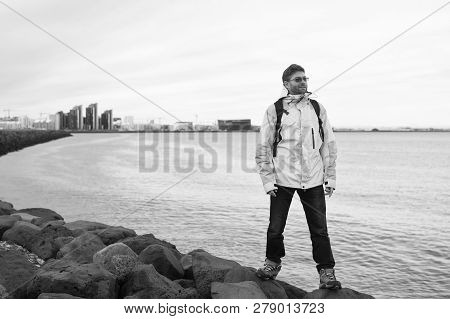 Inspired Man On Sea Beach In Reykjavik, Iceland. Man Traveler Smile And Looking In Future On Sea Sho