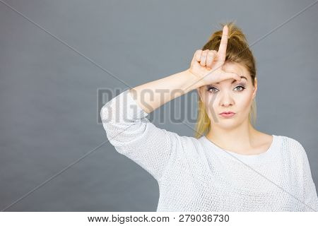 Woman Showing Mean Sign, Lame Or Loser Gesture With L Fingers On Forehead, Grey Background.