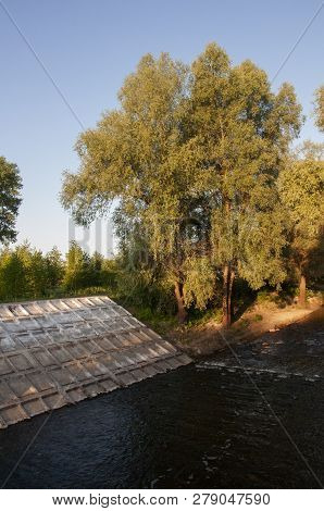 Small River Slow Flowing Across The Green Forest With Reflections Of  Trees In The Water.  Summer