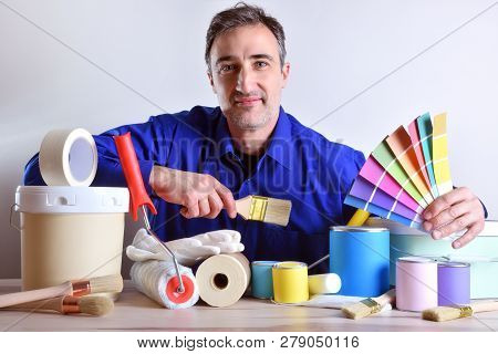 Smiling Worker Presenting Painting Tools And Products On Table. Horizontal Composition. Front View.