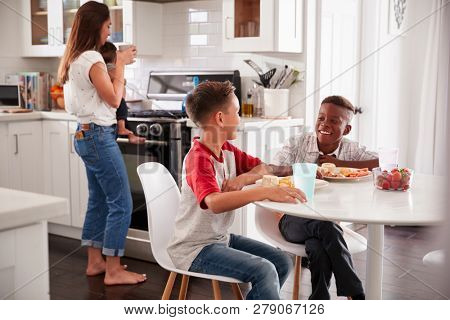 Two pre-teen male friends talk in kitchen at one boyÃâ¢s house, mum holding baby in the background