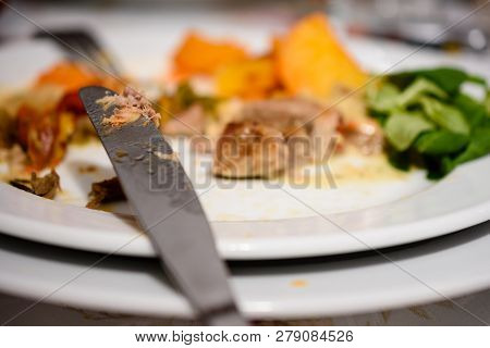 Steel Knife Next To Plate With Partially Consumed Pork Steak With Golden Baked Potatoes And Salad
