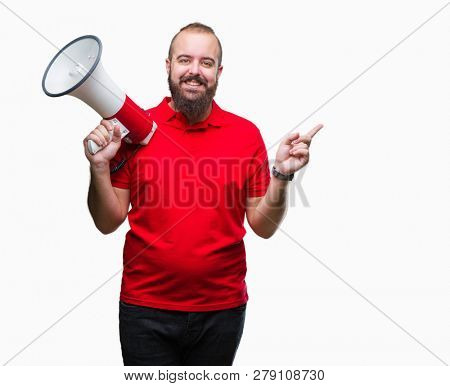 Young caucasian man shouting through megaphone over isolated background very happy pointing with hand and finger to the side