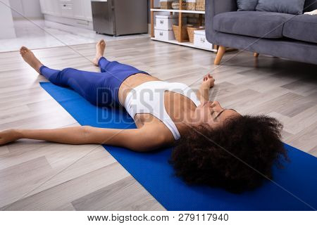 Athletic Young Woman Lying On Blue Yoga Mat Over The Hardwood Floor