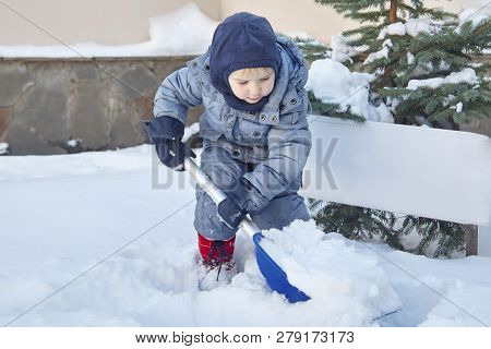 Cute Little Caucasian Baby Boy Shovels Snow In The Yard With Fir-tree On Background. Child With Shov