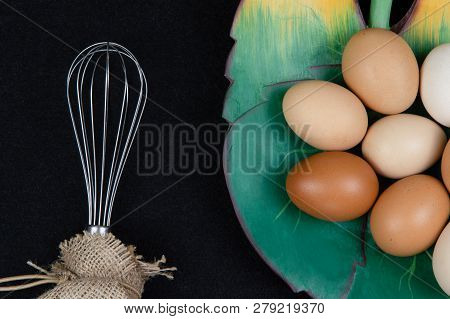 Top View Of Hen Eggs In A Leaf Shaped Plate And An Eggbeater On A Black Background.