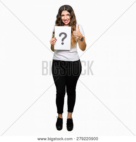 Young adult woman holding paper with question mark happy with big smile doing ok sign, thumb up with fingers, excellent sign