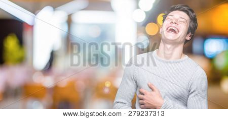 Young handsome man wearing winter sweater over isolated background Smiling and laughing hard out loud because funny crazy joke. Happy expression.