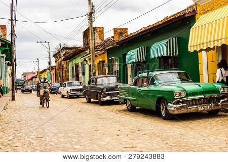 Trinidad, Cuba - 2019.cuban Riding A Bicycle And Old Automobiles Parked In Front Of Colorful Houses