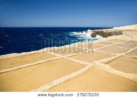 Deep Blue Sea, Horizon And Sky With Yellow-brown Sand Stone Shore Foreground. Salt Ponds In Gozo Isl