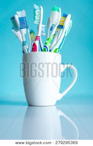 Multi-colored Toothbrushes In A White Mug Close-up In The Bathroom On A Mirror Table On A Blue Backg