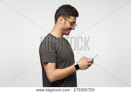 Side Portrait Of Handsome Man Looking At Screen Of Smartphone While Exchanging Messages, Isolated On