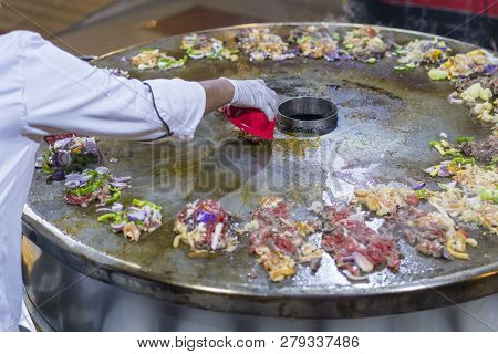 Cooking Street Food On A Large Firebox. Frying Meat And Seafood On The Brazier In The Street. A Cook