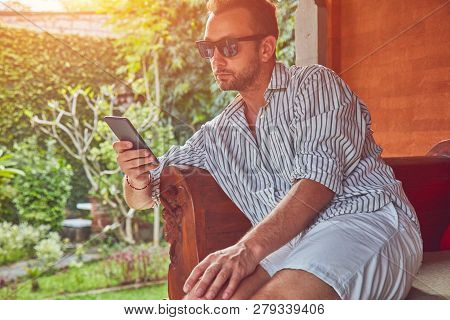 Man Using Smart Phone On A Terrace Sofa In Summertime.