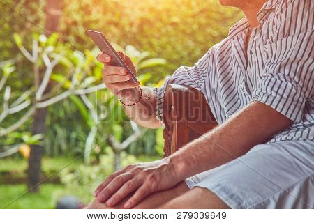 Man Using Smart Phone On A Terrace Sofa In Summertime.