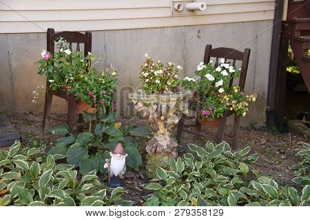 A Beautiful Garden Display With Potted Flower Plants Placed On Chairs And On Top Of A Birdbath With 