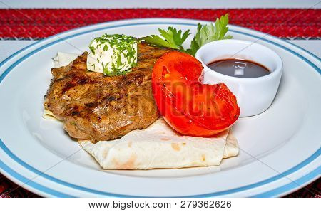 Fried Meat On Pita Bread, With A Slice Of Tomato And Sauce. Served On A Plate.